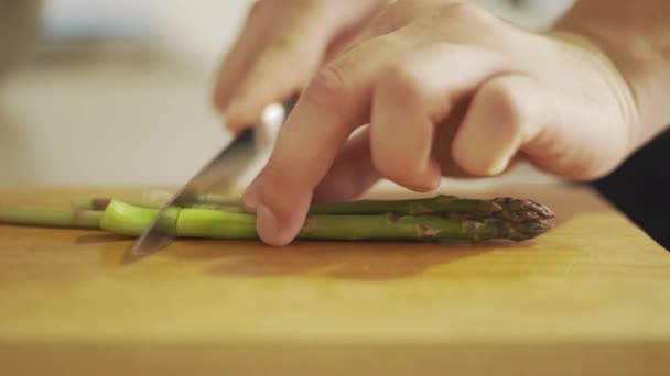 Rauwe groene asperges hakken voor het koken op een houten plank — Stockvideo
