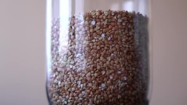 Raw buckwheat groats spinning in a glass jar close up — Stock Video