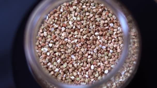 Raw buckwheat groats spinning in a glass jar close up — Stock Video