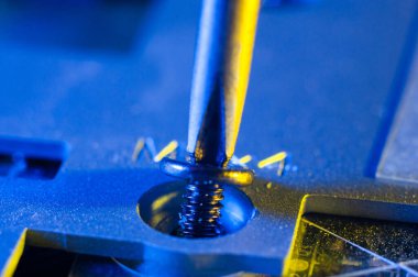 Yıldız tornavidayla küçük bir vidayı sökmek bir dizüstü bilgisayarın yakın plan görüntüsü, sarı-mavi ışıklandırma.