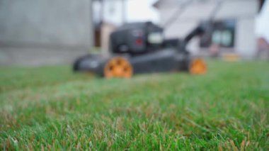Arka taraftaki yeşil çimen ve çim biçme makinesi bulanık arka plan, düzgün kamera hareketi. Bahçede çim biçme işlemi. Yüksek kaliteli FullHD görüntüler