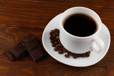 Kahveli içecek ve çikolatalı beyaz bir fincanda, tahta arka planda.