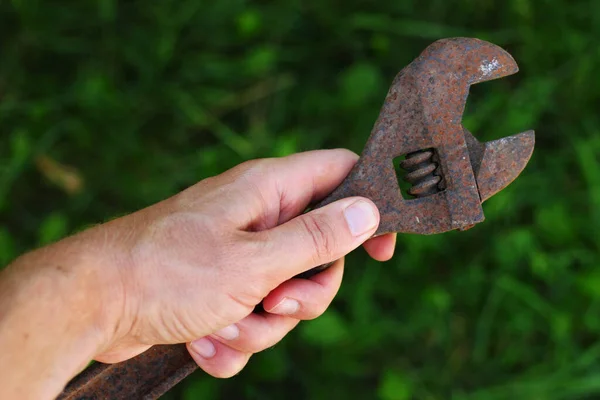 Old adjustable wrench in hand on grass background
