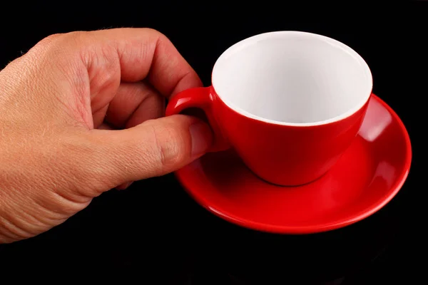 一只手拿着一只空的红色杯子和一只茶托放在黑色的背景上 — 图库照片