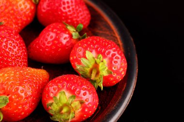 Karanlık bir arka plan üzerine bir tabak içinde çilek