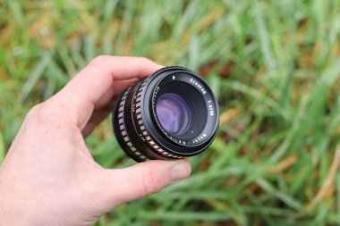 LVIV, UKRAINE - 11 Kasım 2025: meyer optik oreston Bir kişi elinde yeşil çimlerle çevrili bir kamera lensini tutuyor.