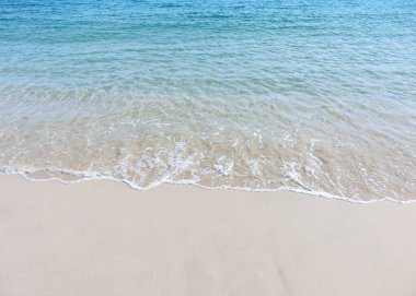 Tropik bir sahilde mavi deniz suyuyla kumlu bir sahilde köpüklü dalgalar.