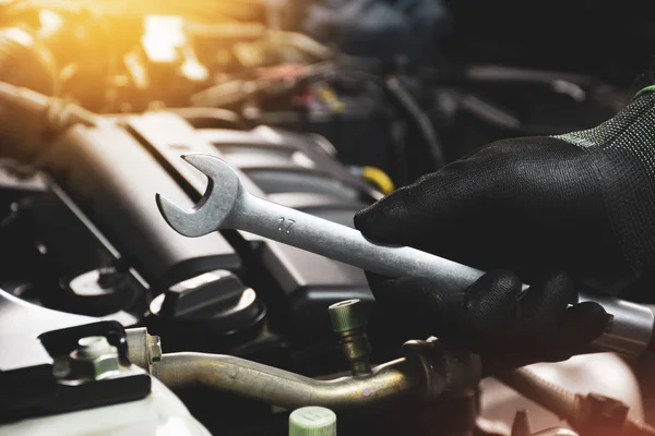 The Mechanic hand wearing black gloves holding open-end wrench with a sunlight and engine blurred on background