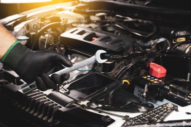 Siyah eldivenler giyen tamirci, arka planda güneş ışığı ve motoru bulanık bir İngiliz anahtarı tutuyor.