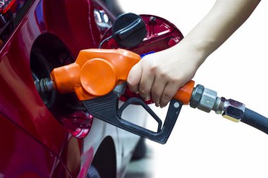 Hand holding pump nozzle is refueling into the fuel tank of a red car