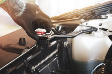 Tamirci el radyatörün soğutucu seviyesini kontrol etmek için radyatör kapağını açıyor.