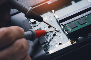 Teknisyen çoklu metre sondayla laptop devre kartını kontrol ediyor