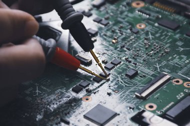 Teknisyen çoklu metre sondayla laptop devre kartını kontrol ediyor