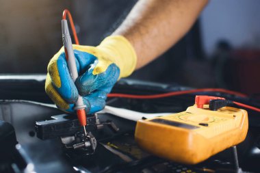 Teknisyen, dijital çoklu metre sondayla araba aküsünü kontrol ediyor.