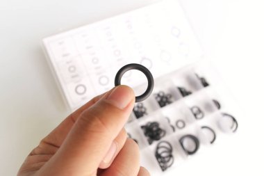 Siyah lastik contalarla dolu temiz bir kutunun üzerinde O halkası tutan bir el. Tesisat tamiri, otomotiv bakımı, DIY projeleri ve donanım organizasyonları için mükemmel..