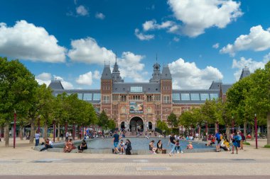 Amsterdam, Hollanda - 23 Temmuz 2020 - Amsterdam şehir merkezindeki Rijksmuseum (federal müze) önünde göletin kenarında oturan turistler