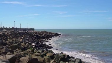 Playa Punta Iglesia La Perla 'da kayalıklara vuran dalgalar, yazın tadını çıkaran turistlerle, Arjantin' in Mar Del Plata kentinde