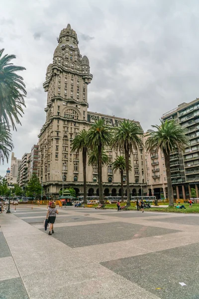 Arka planda ünlü Salvo Sarayı (Palacio Salvo), Montevideo, Uruguay, 25 Ocak 2019 ile Independance Meydanı 'ndan (Plaza Indepencia) geçen turistler
