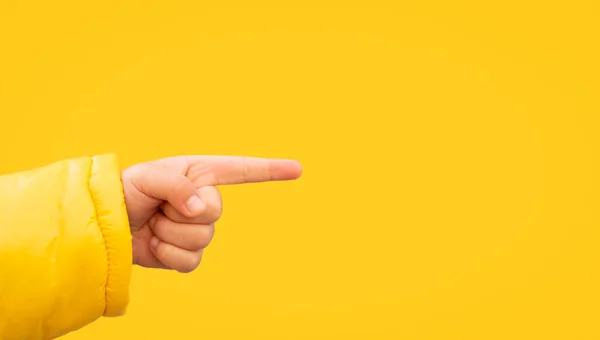 Close up of child hand pointing away on yellow background. Indicating to the side.