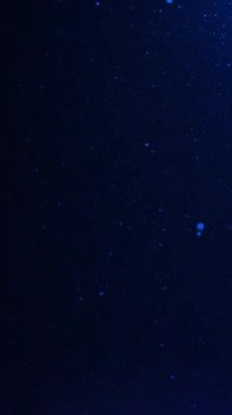 Parlayan güzel mavi parçacıklar yavaşça yükseliyor ve kozmik bir zemin üzerinde yüzüyorlar. Soyut, bilimsel ve teknolojik temalar için ideal