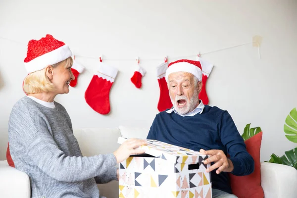 Senior retirement couple with surprise gift during Christmas celebration in their living room