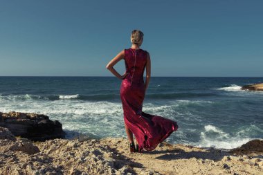 Deniz zemininde poz veren zarif kırmızı elbiseli muhteşem bir manken. Moda konsepti.