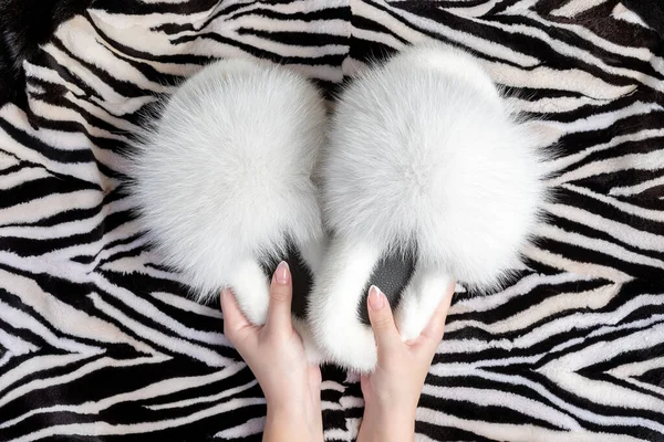 Female hands holding beautiful fur slippers on the fluffy fur plaid. Flat lay.