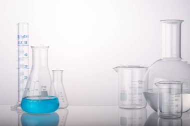 Tıp laboratuarında beyaz arka planda cam mataralar ve silindir şişeler var. Ürün sunumu için alan.