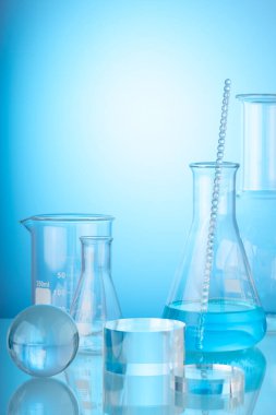 Science and medical background with transparent round podium, lab glassware filled liquid on blue background. Space for products presentation.