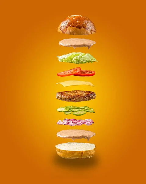 Floating burger ingredients on orange background — Stock Photo, Image