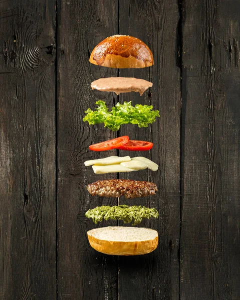 Pływające składniki burger na drewnianym tle — Zdjęcie stockowe