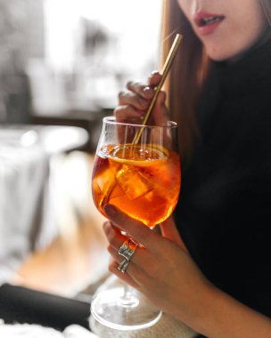 Bir kadın pipetle aperol spreyli kokteyl içiyor.