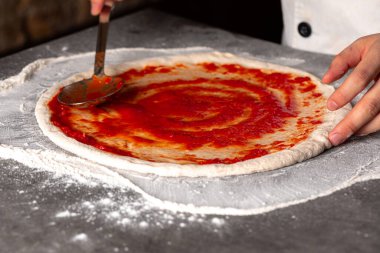 Hamurun üzerine domates sosu serpiştirilmiş pizza yapıyorum.