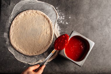 Hamurun üzerine domates sosu serpiştirilmiş pizza yapıyorum.