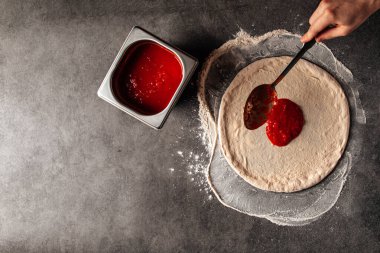 Hamurun üzerine domates sosu serpiştirilmiş pizza yapıyorum.