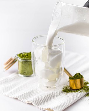 Matcha latte çayı yapmak için bardağa süt döküyorum.