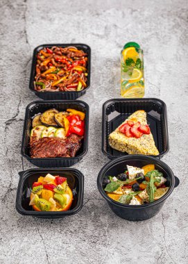 Plastik kaplarda sağlıklı sağlık yemekleri ızgara sebzeler, et, atıştırmalıklar ve gri beton arka planda eritilmiş su.