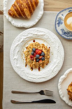 Üzerinde yaban mersini ve ahududu olan sağlıklı yulaf ezmesi. Masada kruvasan ve kapuçino ile servis ediliyor.