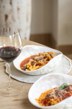 Domates soslu İtalyan makarnası ve beyaz tabakta servis edilen parmesan peyniri ve masada bir bardak kırmızı şarap.