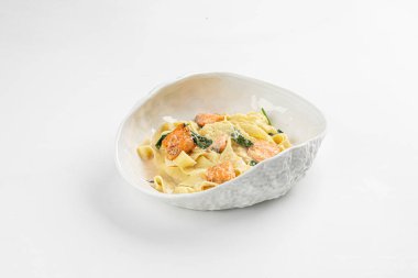 Somon parçalı Tagliatelle makarnası ve beyaz arka planda beyaz kasede servis edilen kremalı soslu ıspanak.
