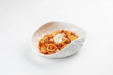 Erimiş peynirle kaplı ve beyaz seramik bir kasede servis edilen yumuşak et parçalarıyla dolu zengin domates soslu spagetti.