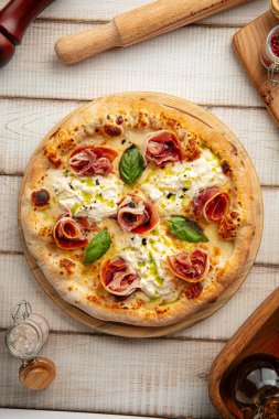 Yeni pişmiş İtalyan pizzası prosciutto, burrata peyniri ve fesleğen yaprakları ahşap tahtada.