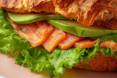 Dilimlenmiş somon, avokado ve kıtır marulla dolu taze kruvasan.