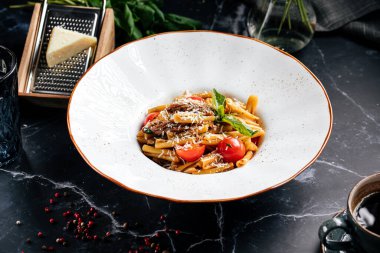 İtalyan makarnası, sebze, rendelenmiş peynir ve taze fesleğen ile servis edilir.