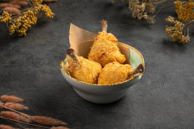 Koyu dokulu arka planda seramik kasede servis edilen çıtır çıtır tavuk budu.