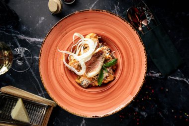 Kurutulmuş balık filetosu, kremalı sos ve renkli bir tabakta taze fesleğenle servis edilen İtalyan makarnası.