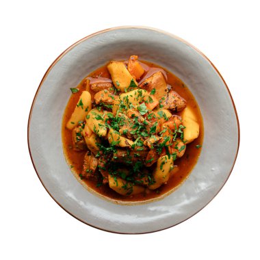 Ayrı aromalı et güveci. Beyaz arka planda, kasede servis edilen patates ve otlarla birlikte.