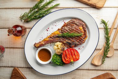 Izgara domates, brokoli ve beyaz tabakta servis edilen soslu pirzola bifteği.