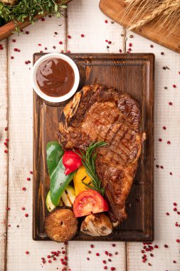 Kızarmış sebze ve ahşap bir tahtanın üstünde barbekü sosuyla servis edilen sulu ızgara biftek.