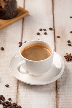 Beyaz seramik bir fincanda servis edilen sıcak sade kahve ve ahşap bir masada baharatlar ve kahve çekirdekleri.